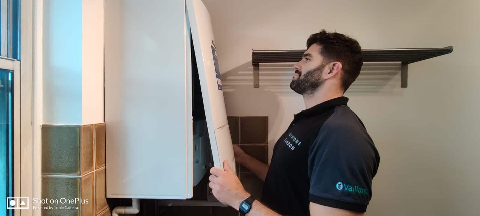 A plumbing and heating engineer stands in front of an open boiler system, examining its internal components.